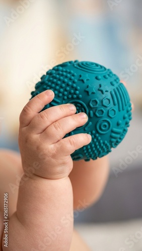 Infant hand grasping textured sensory ball during indoor playtime macro close-up with soft lighting