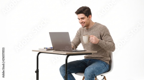 Happy young man sitting at desk using laptop computer and holding cup of coffee isolated on white background