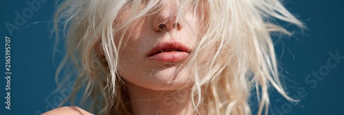 Closeup windblown blonde portrait focusing on lips and hair texture against blue sky for beauty wallpaper and design