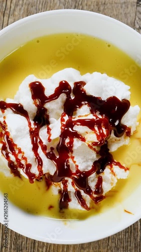 Floating island dessert with meringue custard and caramel sauce on white plate, vertical footage