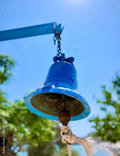 Low angle shot of a classic bright blue metal church bell hanging with a rope against a bright clear blue sky.
