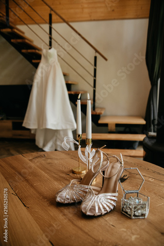 Bride's morning on her wedding day in a hotel room with accessories: wedding dress nearby, festive shoes, box with gold wedding rings, candles in candelabras on the table