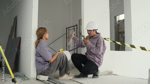 Construction inspector and two site workers in safety helmets discussing building plans with clipboard and caution tape, ensuring teamwork and safety on industrial construction site indoors