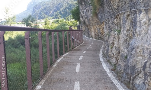 Scenic Asphalt Bike Path Along Rocky Cliff with Metal Safety Railing in Mountain Landscape.

