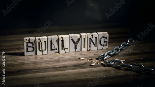 Broken metal chain lying next to wooden blocks spelling the word bullying