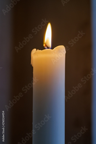 Фотография Burning white devotional candle in a dark church interior