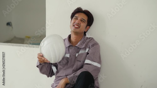 Construction inspector wearing safety helmet and worker uniform on building site showing protection and injury prevention with young male labor in industrial occupation resting indoors with equipment