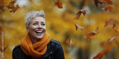 Portrait radiant young woman with short blonde hair, scarf enjoying, laughing joyfully while vibrant autumn leaves fall gently around her in a scenic park during a crisp day in nature