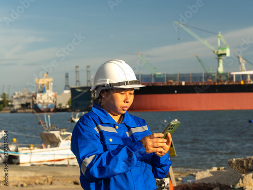 Industrial worker in uniform and hard hat using mobile device at port site