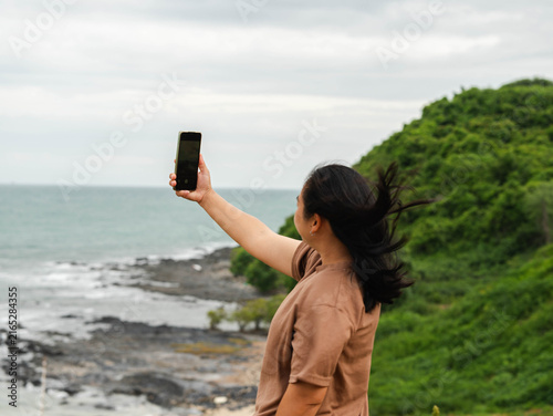 Woman standing at coastal area taking a photo with smartphone