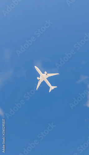 A white commercial airplane flying overhead against a clear blue sky