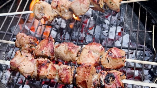 Marinated pieces of meat grilling on metal skewers over a hot charcoal grill in a summer garden with fresh green grass in the background. Close-up barbecue scene with smoky grilled meat