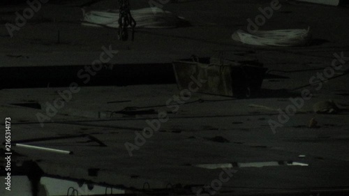 Dark industrial construction scene at night featuring hanging metal chains, rusted container, coiled cables, and debris on concrete surface