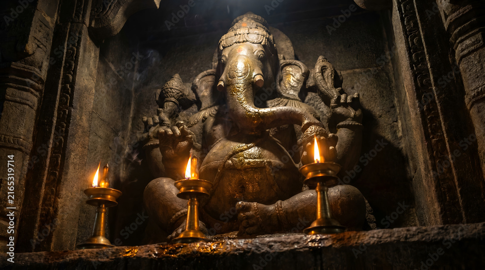 Fototapeta premium Ancient stone Ganesha statue illuminated by soft lamp light in dark temple