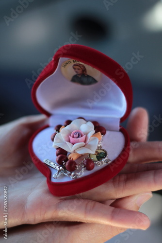 Foto Open red heart velvet case held in hand revealing a handmade rose rosary with a silver cross