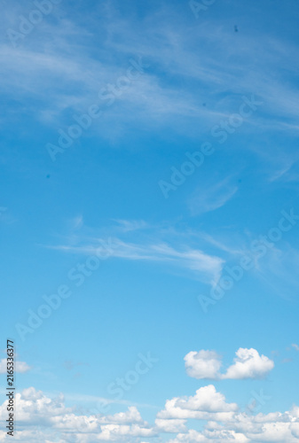 Fotografie Vertical view of a clear blue sky with wispy cirrus clouds and small cumulus clouds near the horizon
