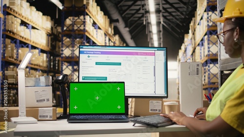Fotografie African American worker follows shipments using tracking information beside copy space in a warehouse with organized shelving and pallets; accurate logistics operations support timely order dispatch