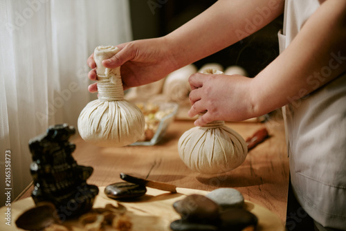 фотографія Hands of female therapist holding herbal compress balls for traditional massage treatment