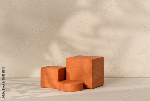 A terracotta textured cube podium paired with a small cylinder pedestal centered on a white surface against a textured beige wall background, offering geometric product display scene