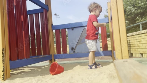 Young child crouching and playing in sand at a colorful playground on a sunny day.