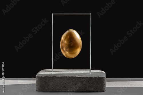 Title: Golden egg inside a transparent acrylic cube on a concrete pedestal