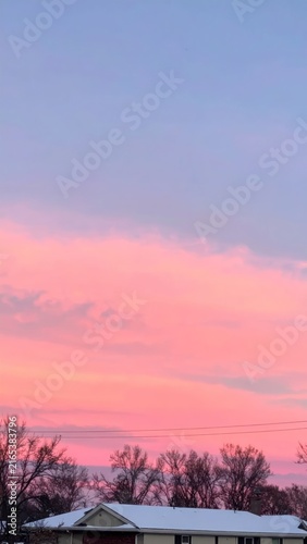 Beautiful pink sunset sky over a snowy house roof.