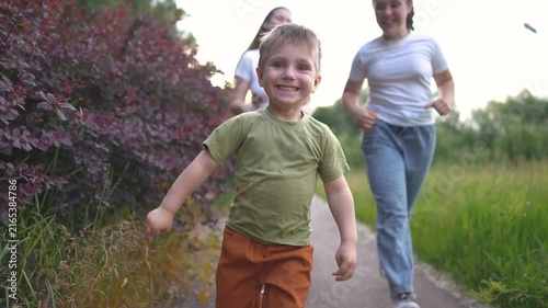 A boy joyfully runs along a path, while two girls run behind him. The boy's laughter echoes as they race through the lush greenery of the park.