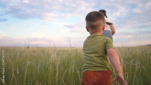 A boy in a green shirt and brown shorts runs through tall grass, as a girl in a white shirt leads the way. The boy and girl play in the open field.