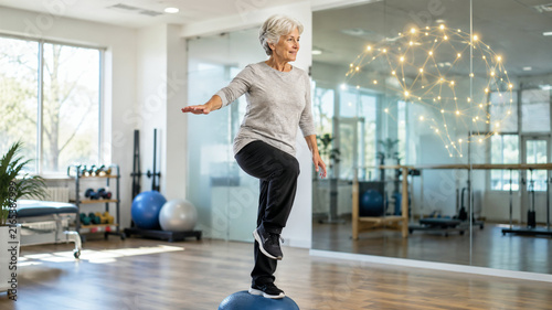 Senior woman training balance on a stability dome in a physiotherapy studio with brain graphic