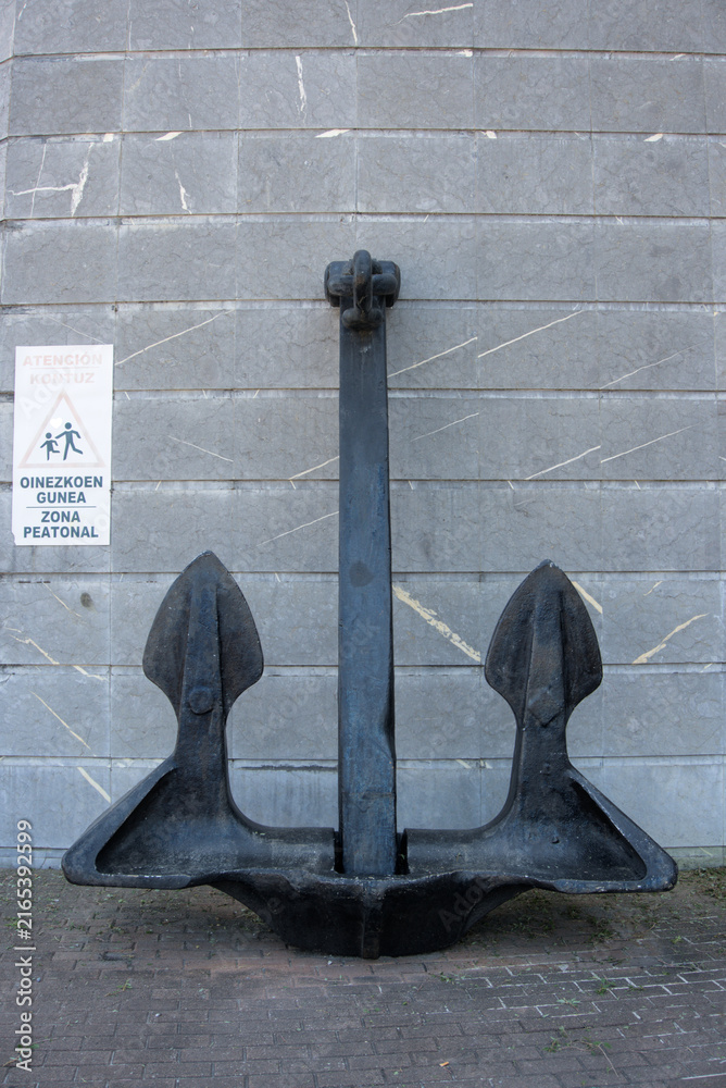 Fototapeta premium Bilbao, Spain - August 12, 2026: A large ship anchor against a grey marble wall on a paved quay