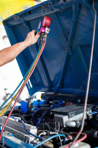 Foto Auto mechanic using a manifold gauge set to check pressure and recharge Freon in a car air conditioning system under the open hood in a garage workshop