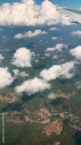 Aerial view from an airplane window looking down at green forested mountains and fluffy white clouds. FHD vertical footage