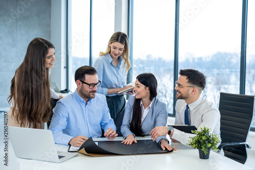 Group of young professionals examining project blueprints and documents together at desk in modern office.