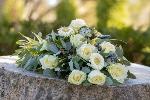 Funeral flower arrangement of yellow and white flowers. Loved ones have left farewell flowers after the interment of the urn. Funeral flowers on a memorial stone in a cemetery. Blurred background.