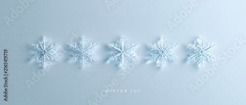 Five transparent glass snowflakes in a row on a light blue background. Minimalist winter holiday 