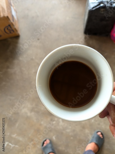 Obraz na plátně Top view of a cup of black coffee served in a white ceramic cup, held by hand in