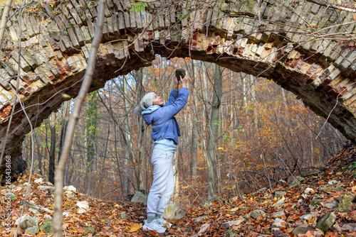 Canvastavla Adult woman holds a fallen masonry block while looking upward at an old deteriorating brick arch in a deciduous autumn forest