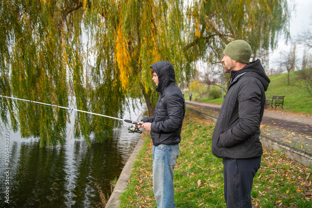 Naklejka premium Father and Son Fishing Together by a Lake in Autumn Park
