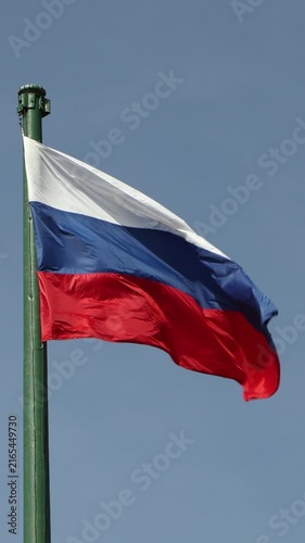 Russian national flag waving on flagpole against clear blue sky. Vertical