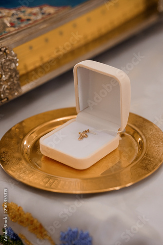 Small golden cross necklace in a white velvet jewelry box on a brass plate next to a sacred book.