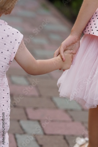 Two Young Girls Holding Hands on a Colorful Paved Walkway in Pink and White Polka Dot Dresses