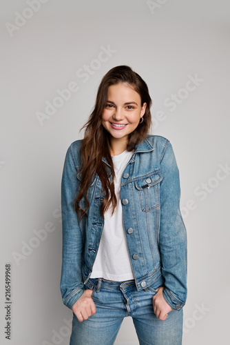 A cheerful teenage girl poses confidently in a denim jacket, white shirt, and jeans
