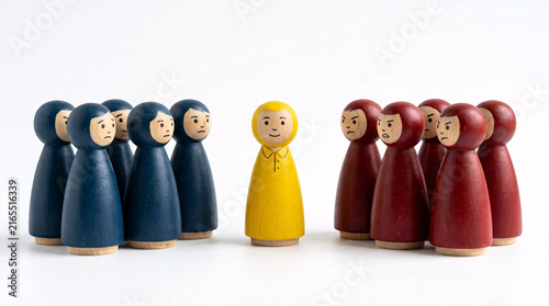 A group of blue and red wooden figures stand facing a single yellow figure, symbolizing separation or individuality within a collective.