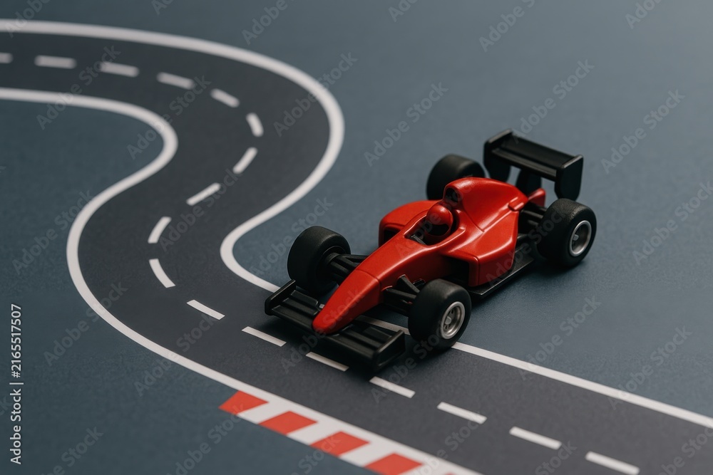 Naklejka premium A red toy Formula 1 race car on a miniature winding racetrack with marked lanes and curbs.
