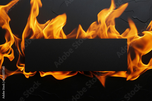 Fiery flames engulf a black rectangular sign against a dark textured background.