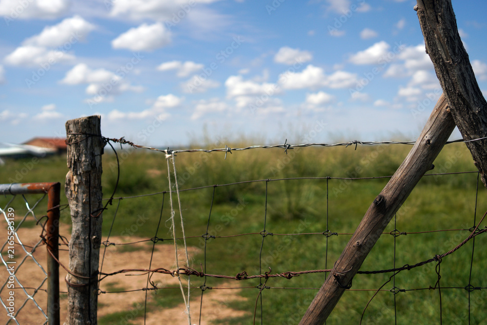 Fototapeta premium Wooden Fence and Barbed Wire Under Bright Blue Sky