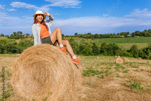 Foto Adventurous young woman shielding her eyes atop a hay bale, scanning the countryside horizon as if spotting something in the distance