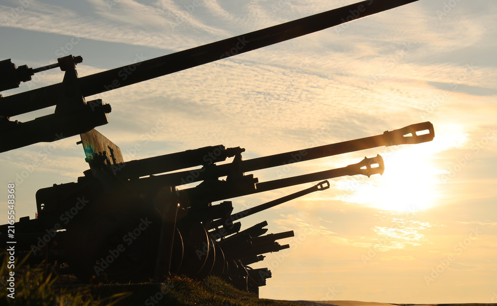 Fototapeta premium Cannons silhouetted against a stunning sunset, the scene exudes a sense of historical grandeur strength. positioned in a row perspective, bathed in the warm glow of the setting sun World war II 2 two