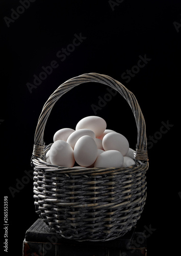 white eggs in wicker basket on black background