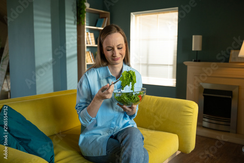Bild auf Leinwand Woman sitting on a yellow sofa at home, frowning and showing strong dislike for